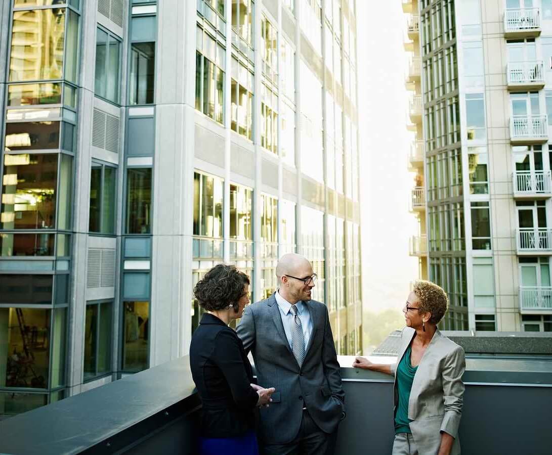Business leaders meeting on a rooftop terrace with a city skyline in the background.