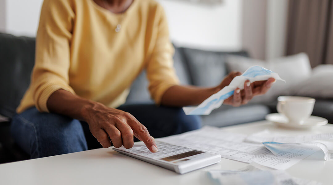 Person reviewing household bills and calculator at a table.
